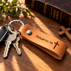 SANTJAG personalized tan leather keychain engraved with Psalm 91:10 and a Christian cross, displayed with metal keys, a Holy Bible and warm natural lighting.