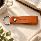 Cognac leather keychain engraved with Psalm 91:10 and a cross, with silver hardware beside an open Bible and coffee.