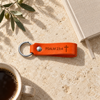 Orange leather keychain engraved with Psalm 23:4 and a cross, displayed on a stone surface beside olive branches and a book.