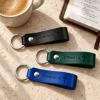 Black, green and blue leather keychains engraved with John 10:10, Joshua 1:9 and Isaiah 41:10 beside an open Bible.