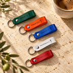Green, orange, blue, white and red leather Bible verse keychains arranged diagonally beside coffee and olive branches.