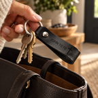 Hand holding a black leather keychain engraved with John 10:10 and a cross, with keys above an open black handbag.