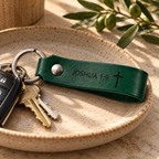 Green leather keychain engraved with Joshua 1:9 and a cross, attached to keys and a car remote on a ceramic tray.