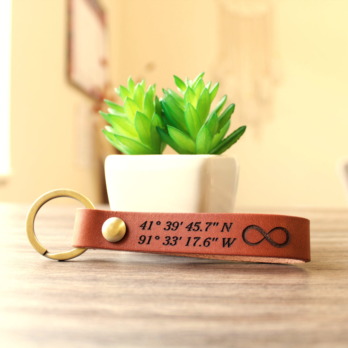 Custom full-grain leather coordinates keychain in cognac brown with laser engraved GPS location coordinates and compass symbol on front and personalized message on back with solid screw metal hardware ring.