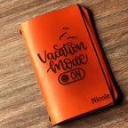 Personalized brown full-grain leather passport cover with laser engraved Vacation Mode On design, elastic band closure, and custom name Nicole engraved at bottom corner.
