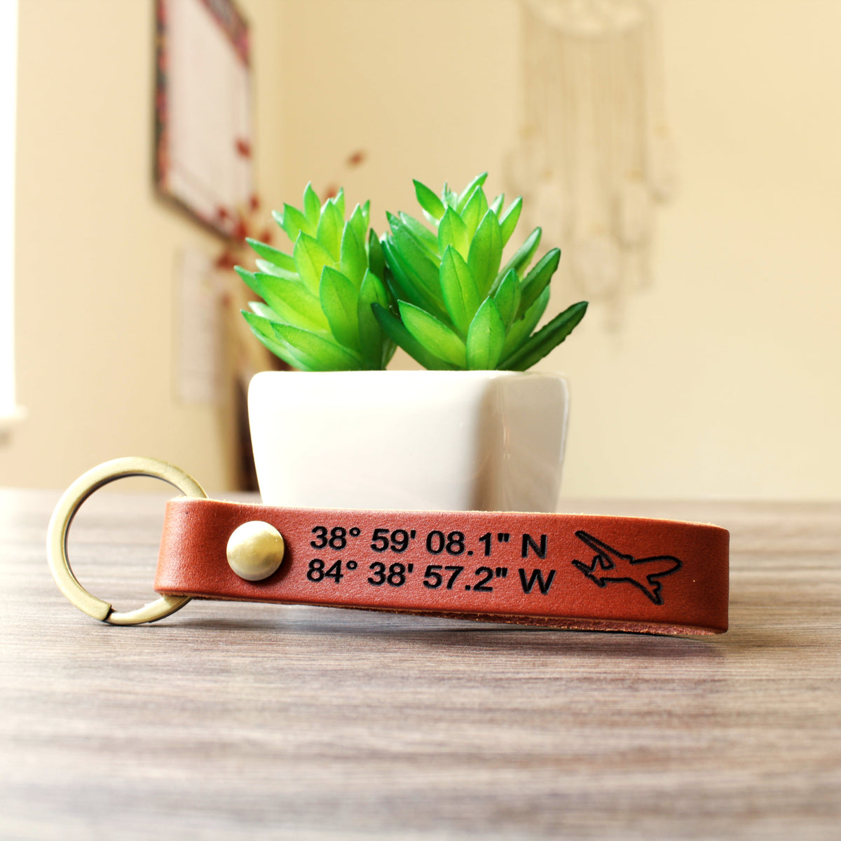Custom full-grain leather coordinates keychain in cognac brown with laser engraved GPS location coordinates and compass symbol on front and personalized message on back with solid screw metal hardware ring.