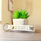 Custom full-grain leather coordinates keychain in cognac brown with laser engraved GPS location coordinates and compass symbol on front and personalized message on back with solid screw metal hardware ring.